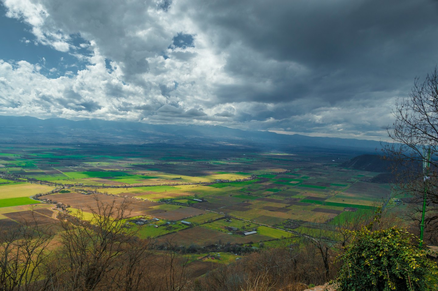 Sunbeams illuminate a valley of fields, roads, and buildings near mountains.
